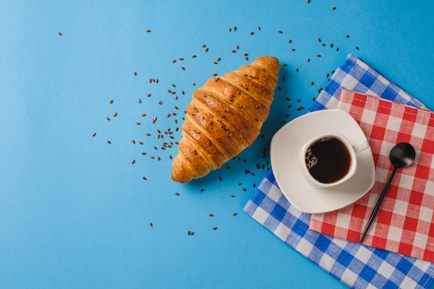 Café con un croissant sobre un fondo azul.