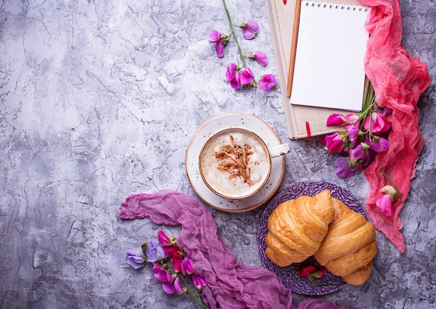 Café, croissants, flores e notebook.