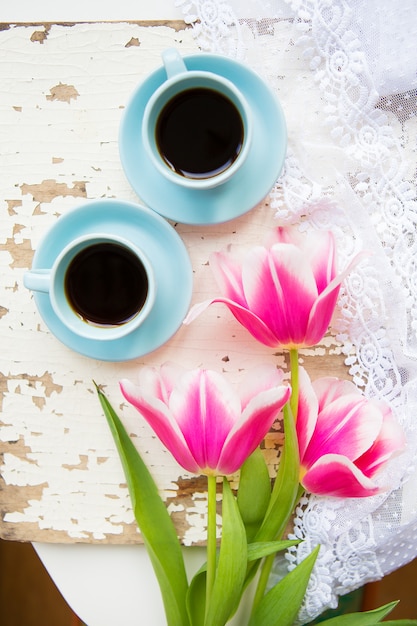 Café, croissants y tres hermosos tulipanes rosados en la vieja mesa blanca