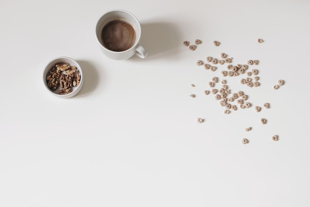 Café da manhã ainda vida Aveia mel crocante ou cereais em forma de coração de trigo sarraceno isolados no fundo da mesa branca Xícara de café com nozes Lanche saudável Comida vegetariana Bebida Vista superior plana leiga