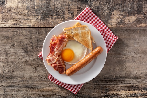 Café da manhã americano tradicional com ovo frito, torradas, bacon e salsicha na mesa de madeira