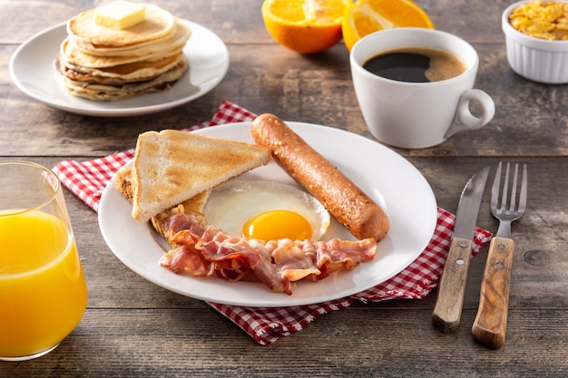 Café da manhã americano tradicional com ovo frito, torradas, bacon e salsicha na mesa de madeira