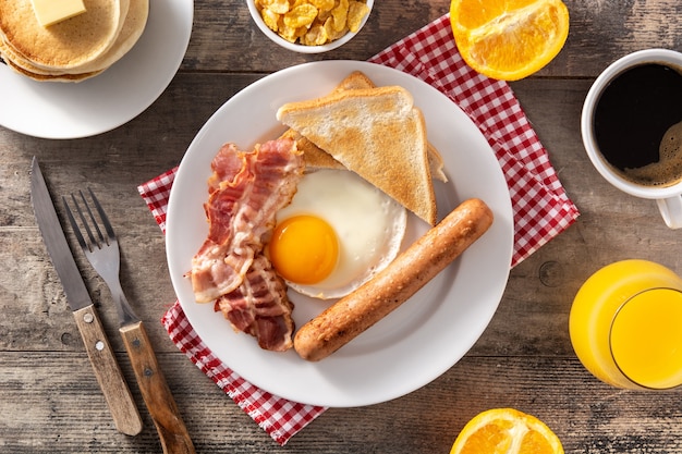 Café da manhã americano tradicional com ovo frito, torradas, bacon e salsicha na mesa de madeira