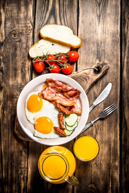 Café da manhã. bacon frito com ovos e suco de laranja. em uma mesa de madeira.