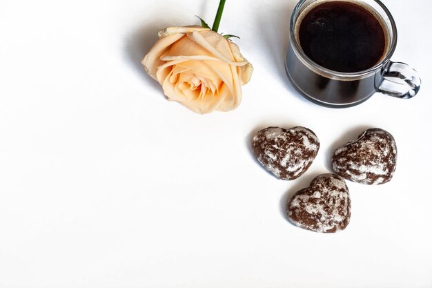 Café da manhã, café, bolos de chocolate em forma de coração e uma rosa amarela em um fundo branco, copie o espaço