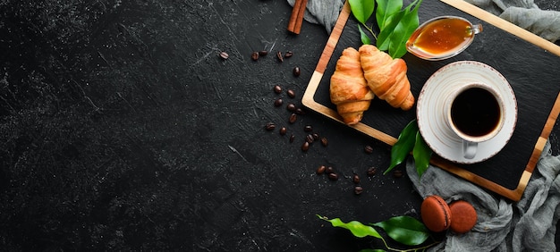 Café da manhã. Café, croissant e macarons. Em um fundo de pedra preta. Vista do topo. Espaço livre para o seu texto.