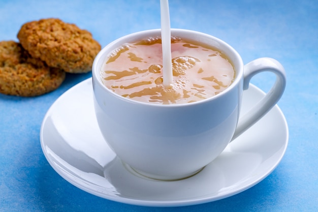 Café da manhã com biscoitos de aveia e derramar leite em uma xícara de chá preto. farinha, sobremesa de cereais e bebida quente