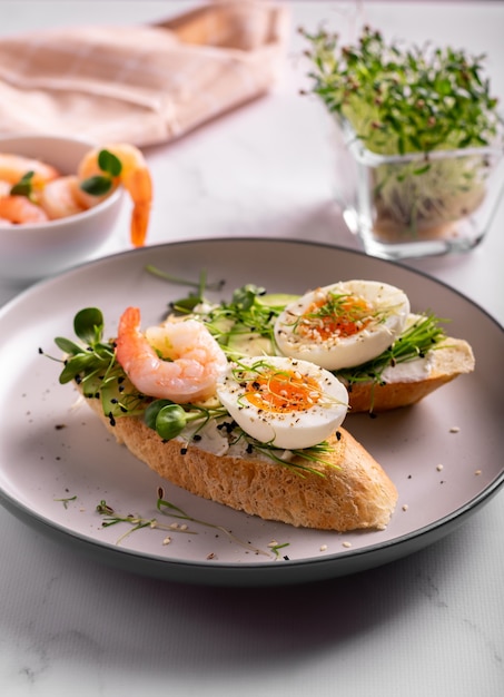 Café da manhã com bruschetta com camarões, ovos e microgreens em um prato, close-up