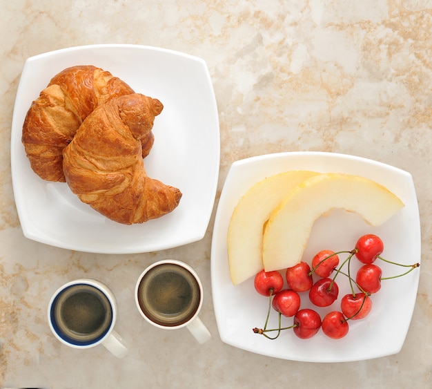 Foto café da manhã com café, croissants e frutas - melão, cerejas