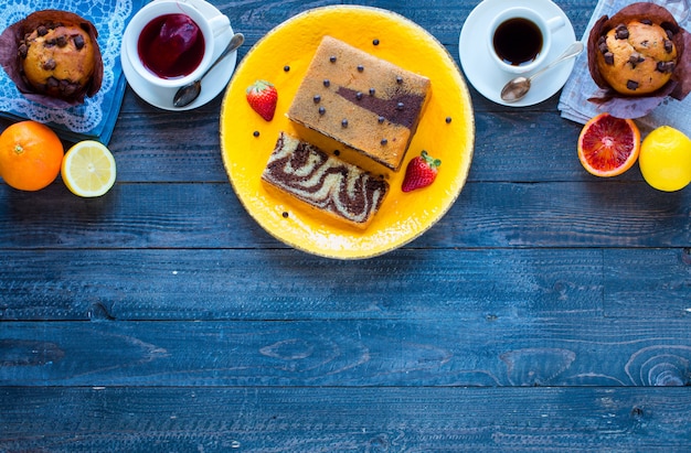 Café da manhã com café e chá com diferentes bolos e frutas em uma mesa de madeira