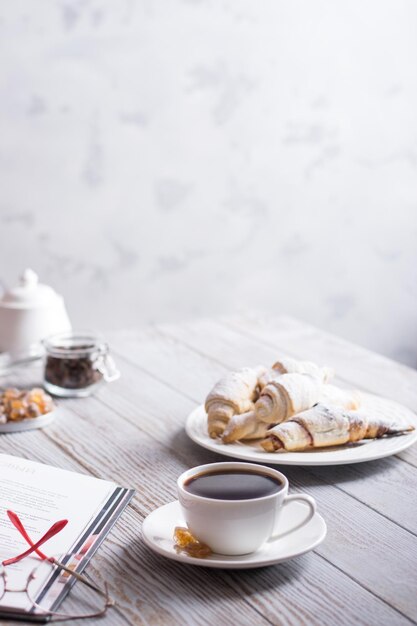 Foto café da manhã com café e croissants enquanto lê um livro