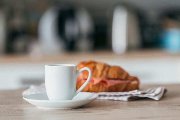 Café da manhã com café e sanduíche de croissant recheado com salame na cozinha