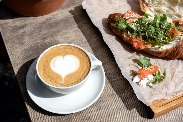 Foto café da manhã com cappuccino e pão no café. manhã americana. croissant com truta e rúcula