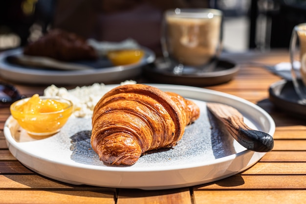 Café da manhã com croissant, geléia de laranja e manteiga com cappuccino em café ao ar livre manhã ensolarada