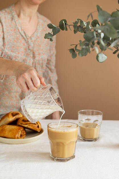 Café da manhã com leite em um copo com pãezinhos de canela com uma mulher derramando creme estilo rústico