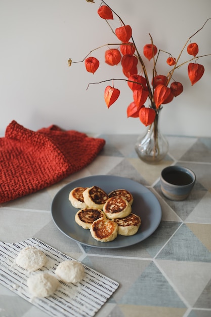 café da manhã com panquecas caseiras de queijo cottage, uma xícara de chá e flores em um vaso sobre a mesa