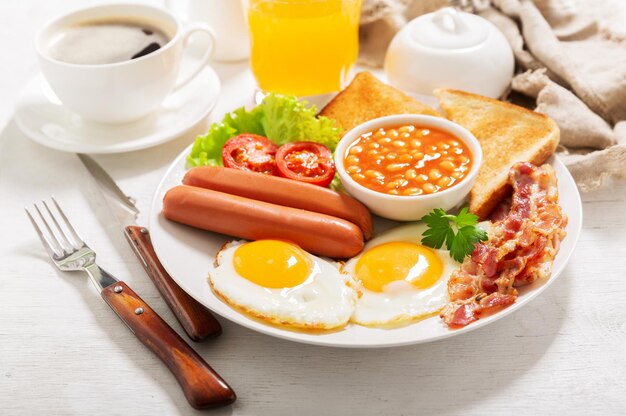 Café da manhã com prato de ovos fritos bacon feijão salsichas torradas e tomates