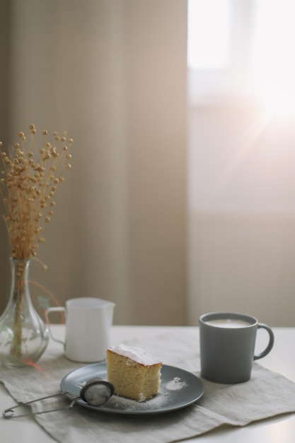 Café da manhã com um pedaço de bolo caseiro fresco, jarro e xícara de café em uma mesa.