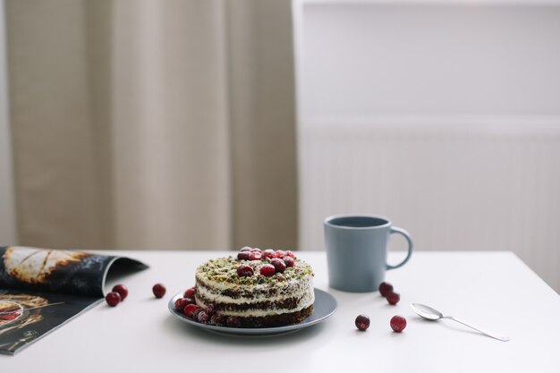 café da manhã com xícara de chá e bolo com espinafre e creme decorado com cranberries frescas na mesa branca