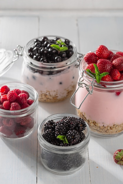 Café da manhã comida saudável. Iogurte de granola com morango caseiro, mirtilo, amora e framboesa em frasco de vidro na cozinha de casa