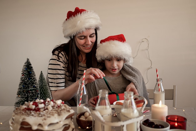 Foto café da manhã de natal feliz. mamãe dá um presente para o filho. menino sorridente desembrulha um presente.