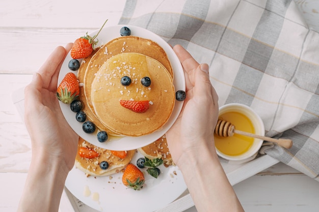 Café da manhã de panqueca para crianças com frutas vermelhas e mel em forma de um rosto sorridente