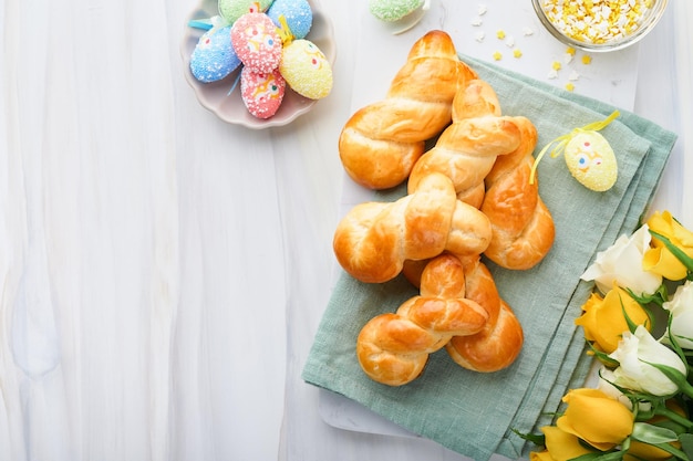 Café da manhã de Páscoa Holliday conceito Pãezinhos de coelhinho da Páscoa com canela feita de massa de fermento com esmalte laranja decorações de páscoa ovos coloridos em fundo branco de primavera Cartão de Páscoa Holliday