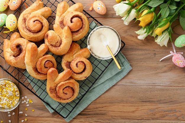 Café da manhã de Páscoa Holliday conceito Pãezinhos de coelhinho da Páscoa com canela feita de massa de fermento com esmalte laranja decorações de páscoa ovos coloridos em fundo de madeira velho Cartão de Páscoa Holliday