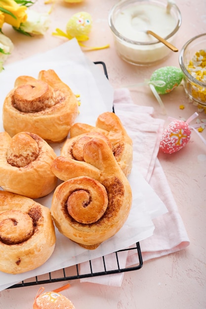 Café da manhã de Páscoa Holliday conceito Pãezinhos de coelhinho da Páscoa com canela feita de massa de fermento com esmalte laranja decorações de páscoa ovos coloridos no fundo rosa da primavera Cartão de Páscoa Holliday