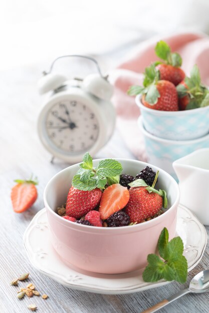 Café da manhã de primavera com granola e morangos frescos e lichia e flores sobre fundo de madeira.