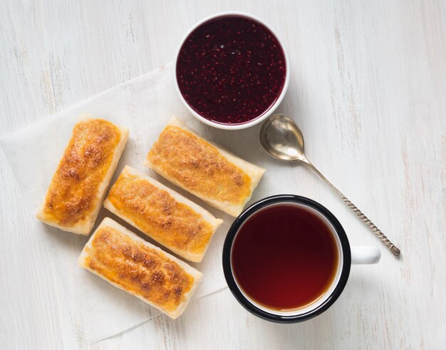 Café da manhã de rolos doces de massa folhada, geléia de framboesa, xícara de chá em papel pergaminho.