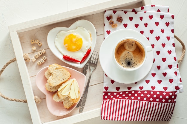 Café da manhã do dia das mães. bandeja há uma xícara de café dois pratos de ovos mexidos e pão em forma de coração e a inscrição eu te amo mãe vista de cima