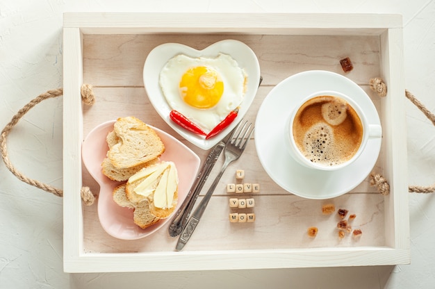 Café da manhã do dia das mães. bandeja há uma xícara de café dois pratos de ovos mexidos e pão em forma de coração e a inscrição eu te amo mãe vista de cima