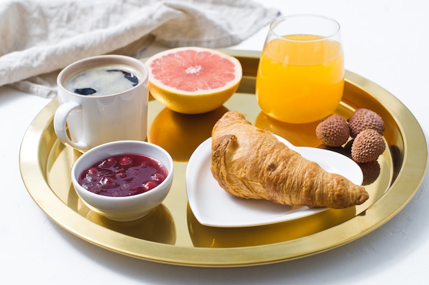 Café da manhã do francês em uma bandeja dourada, café, doce, croissant, suco de laranja, toranja, lichi.