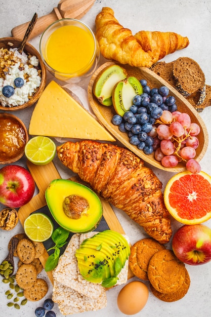 Café da manhã equilibrado saudável no fundo branco. Muesli, suco, croissants, queijo, biscoitos e frutas, vista superior.