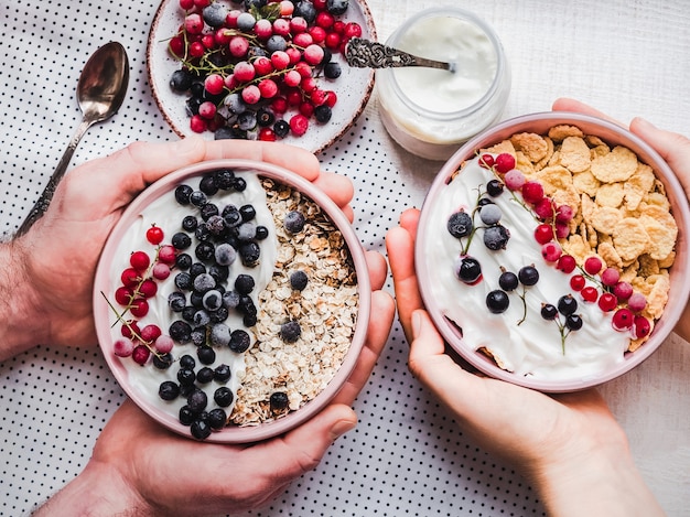 Café da manhã festivo e saudável para seus entes queridos. taças vintage, flocos de milho, granola, iogurte, frutas frescas e mãos de um jovem casal.