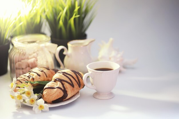 Café da manhã francês na mesa. Croissant de café com chocolate e um decantador com creme. Pastelaria fresca e café descafeinado.