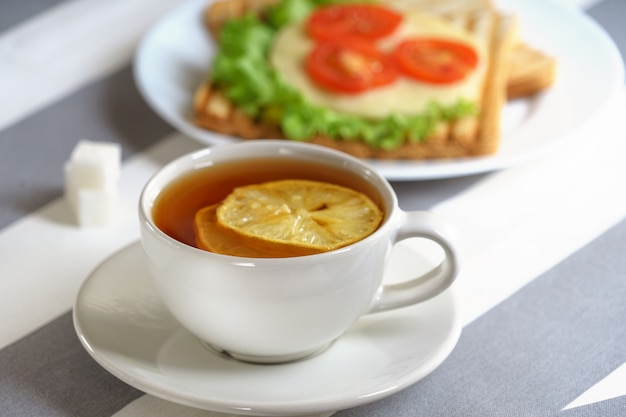 Café da manhã fresco, saboroso com um sanduíche e chá em um fundo claro.