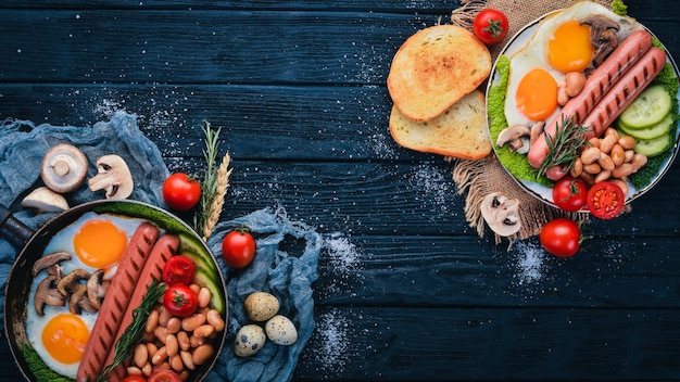 Café da manhã inglês completo com ovos fritos, salsichas, feijão, torradas e café no fundo do espaço de cópia. Em um fundo preto de madeira.