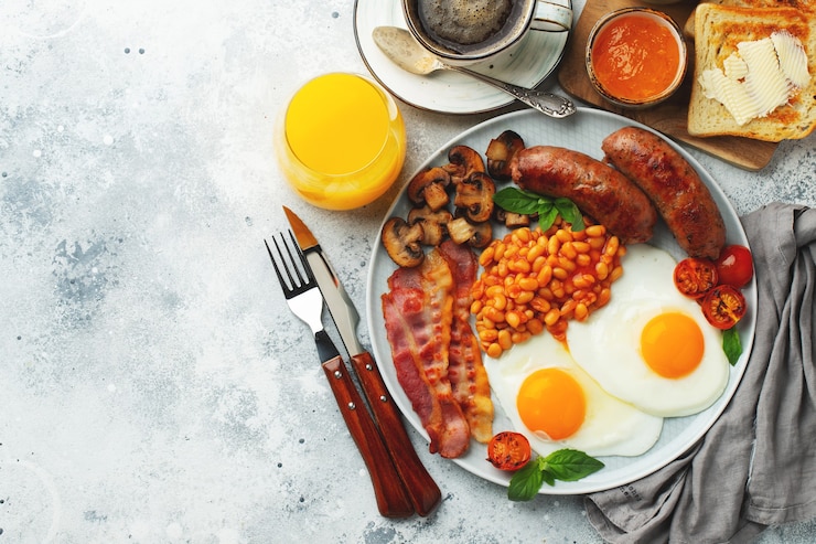 Foto café da manhã inglês completo em prato com ovos fritos, linguiça, bacon, feijão, torradas e café. vista de cima.