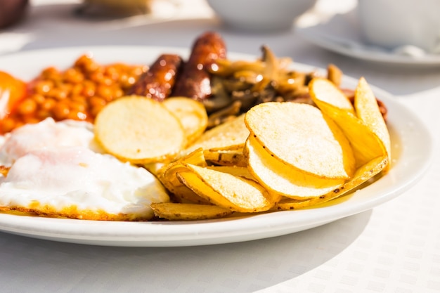 Café da manhã inglês completo, incluindo salsichas, tomates e cogumelos, ovo, bacon, feijão cozido e batatas fritas.