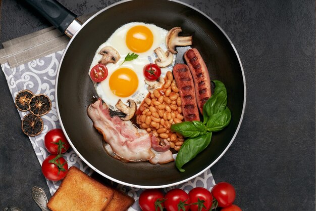 Café da manhã inglês. Ovos fritos, salsichas, bacon, feijão, torradas, tomates na mesa de pedra. Vista superior com espaço de cópia