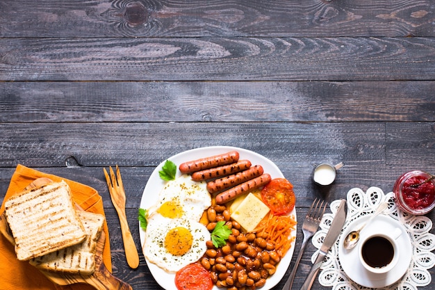 Café da manhã inglês. ovos fritos, salsichas, feijões, torradas de pão, tomate, queijo em um fundo de madeira,