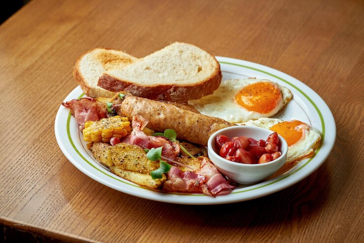 Foto café da manhã inglês - ovos mexidos com bacon, feijão e salsicha em um prato branco sobre um fundo de madeira