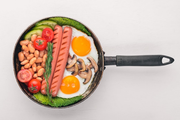 Café da manhã inglês tomates salsichas feijão cogumelos ovos torradas e ervas vista superior sobre um fundo branco de madeira