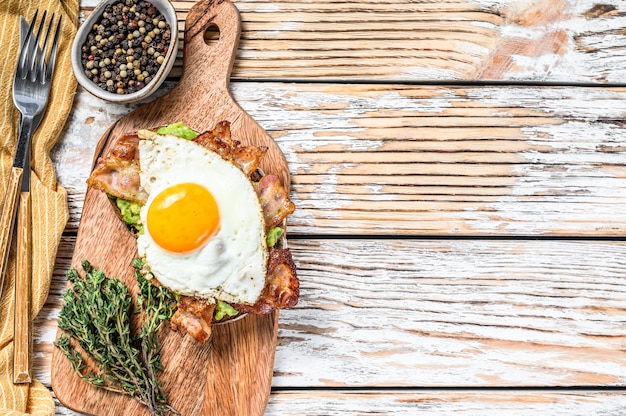 Café da manhã inglês, torradas com bacon, abacate e ovo em uma tábua de cortar.