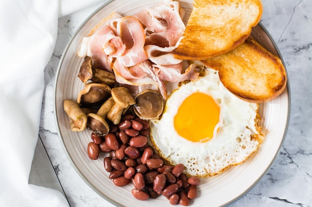 Café da manhã inglês tradicional com cogumelos de feijão de bacon de ovo e torradas em um prato Vista superior