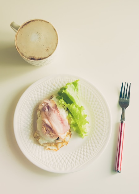 Café da manhã keto com bacon, ovos fritos, salada verde e xícara de café com leite na mesa de madeira branca. conceito de gorduras saudáveis
