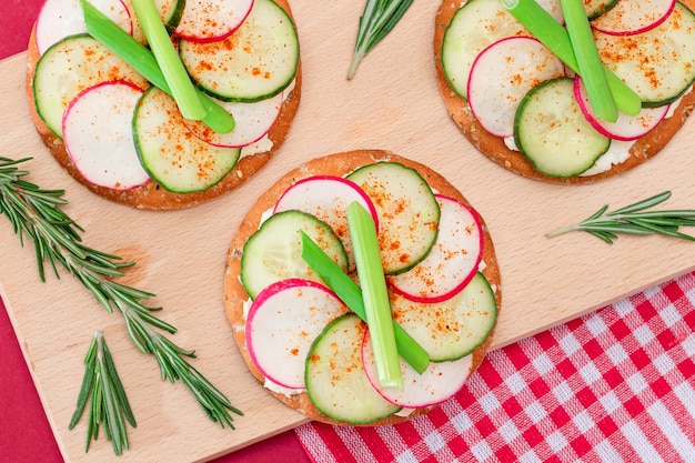 Café da manhã leve ou dieta comendo sanduíche de biscoito crocante com cream cheese pepino fresco cebolas verdes e rabanete na placa de cozinha de madeira em fundo magenta