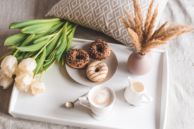 Café da manhã na cama com uma xícara com cappuccino, rosquinhas e tulipas brancas